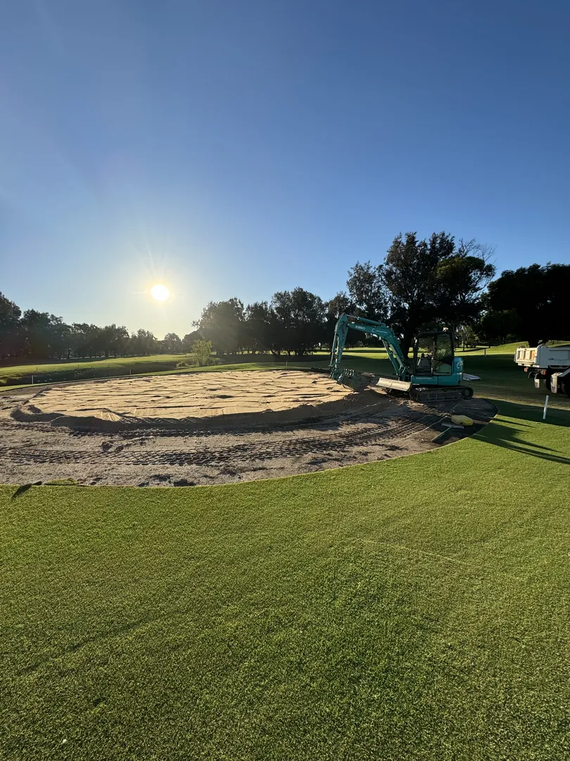 Excavator working on golf course under sunrise