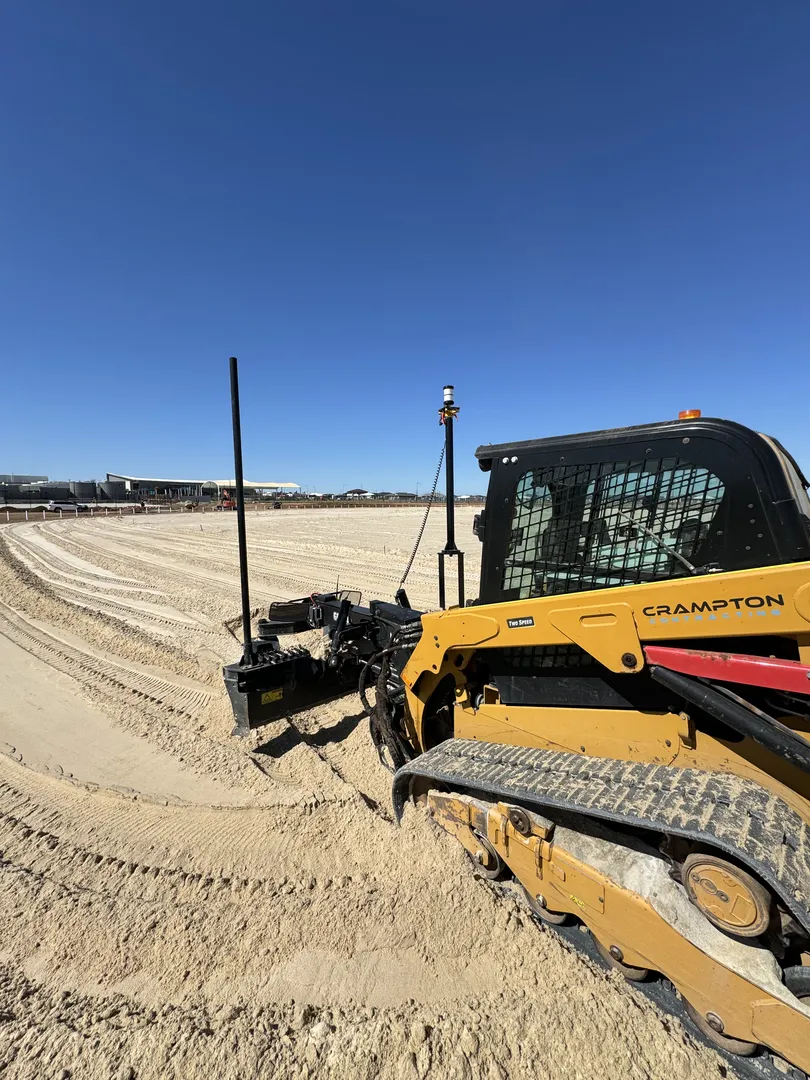 Construction equipment leveling sandy ground on a clear day.