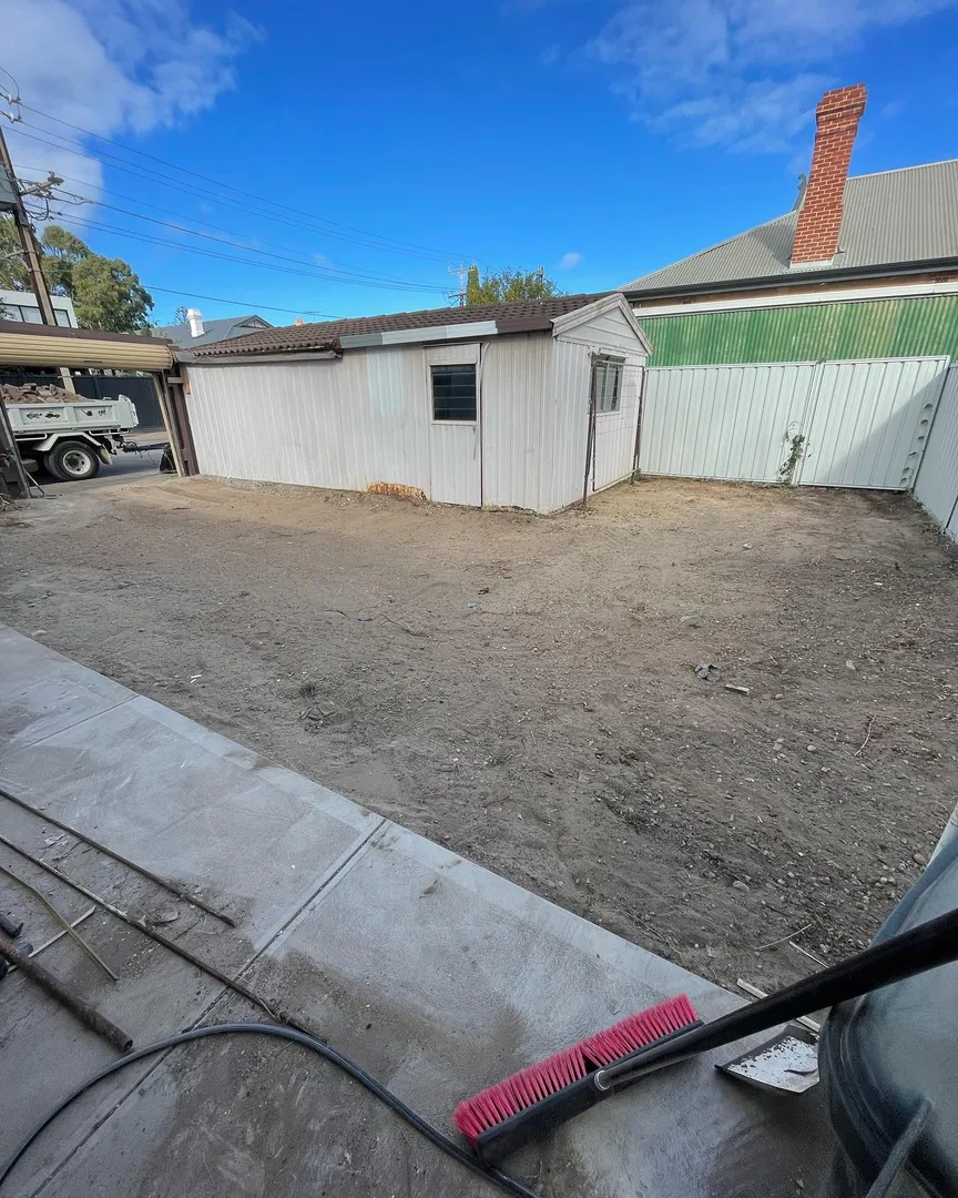 Empty backyard with shed and broom on ground.